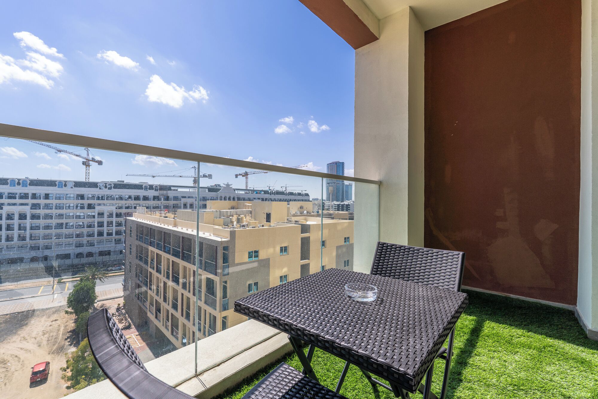 A balcony with a table and chairs, a view of buildings, and a construction crane in the distance.