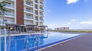 A rooftop swimming pool with clear blue water, surrounded by a wooden deck and lounge chairs. - NEW Lisiting | Miracle Garden | Great Location (Dubai)