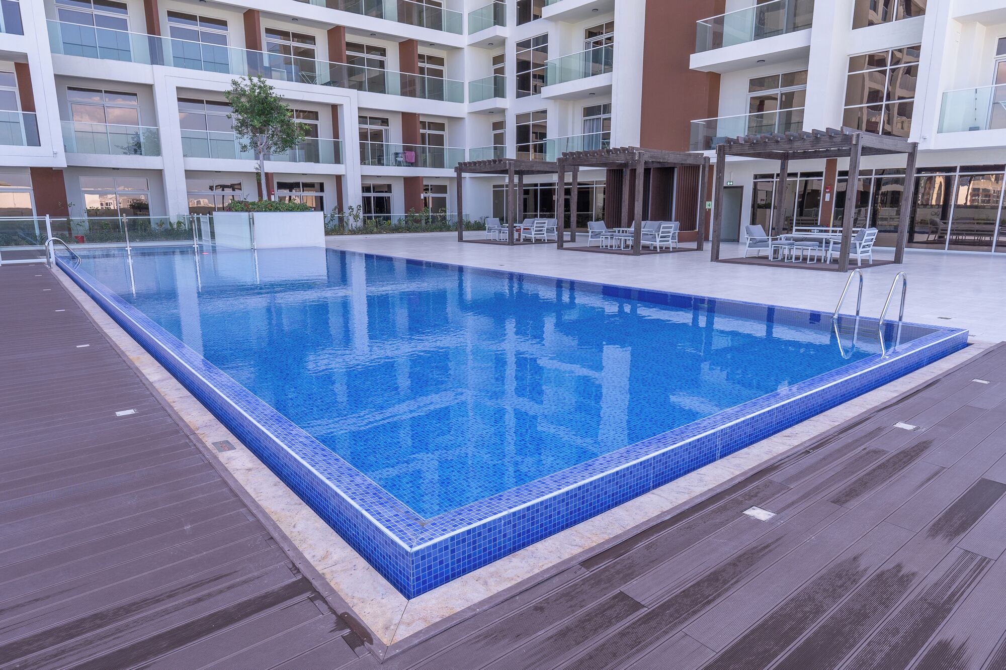 A rectangular swimming pool with blue tiles, surrounded by a wooden deck.