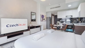 A hotel room with a bed, a TV, a desk, a chair, a small table, and a kitchen area with a stove and microwave. - NEW Lisiting | Miracle Garden | Great Location (Dubai)