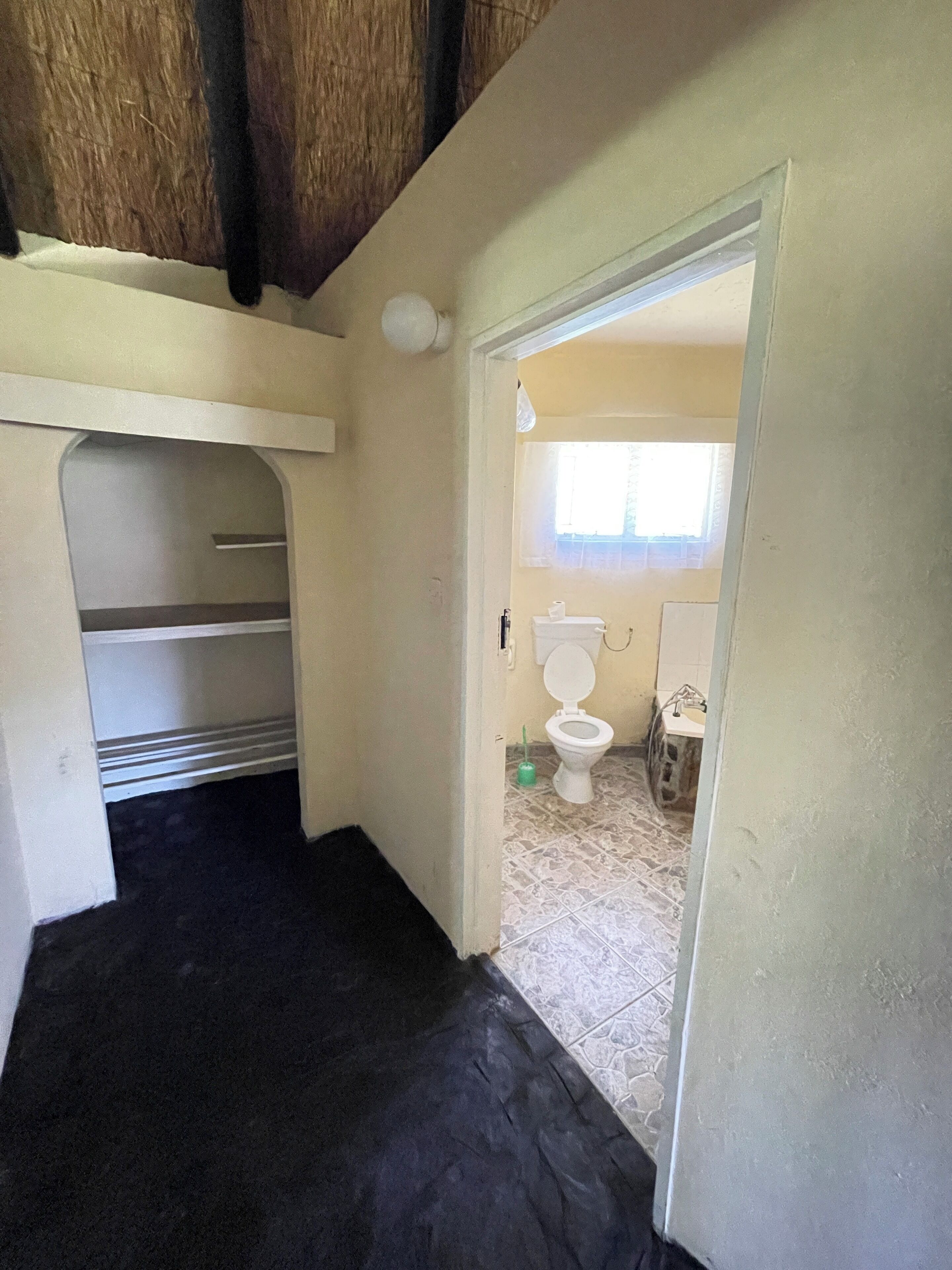 Un pasillo estrecho con piso negro que conduce a un baño con inodoro y lavamanos.