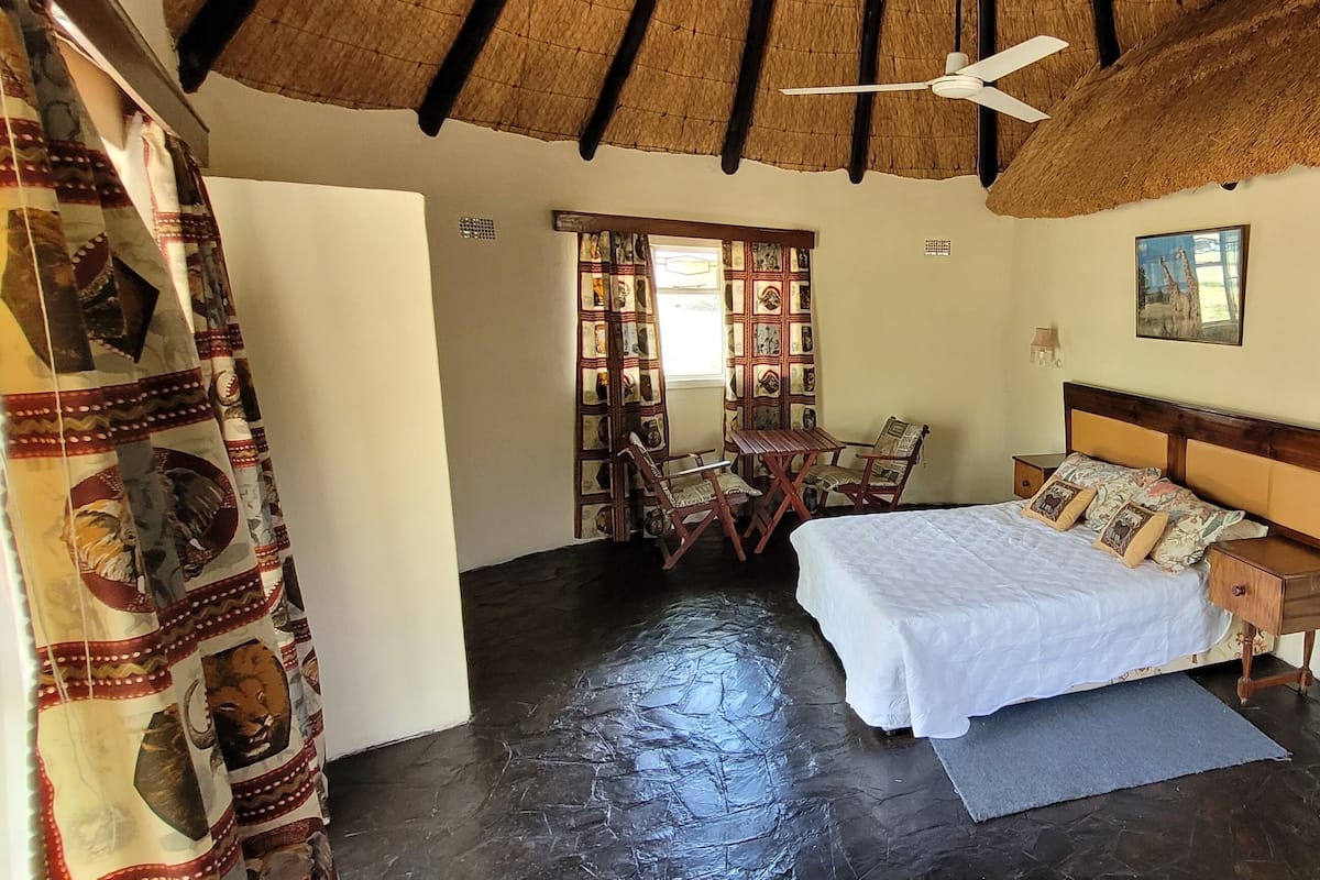 A bedroom with a bed, wooden nightstands, a ceiling fan, a window with a view, and a door with a curtain.