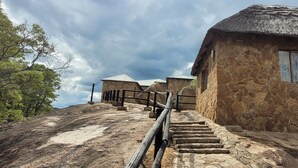 Un edificio in pietra con tetto di paglia, una scala che conduce all'ingresso e vista sul paesaggio circostante.