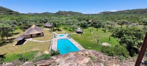 Una piscina rodeada de chozas con techo de paja en un paisaje verde y exuberante.