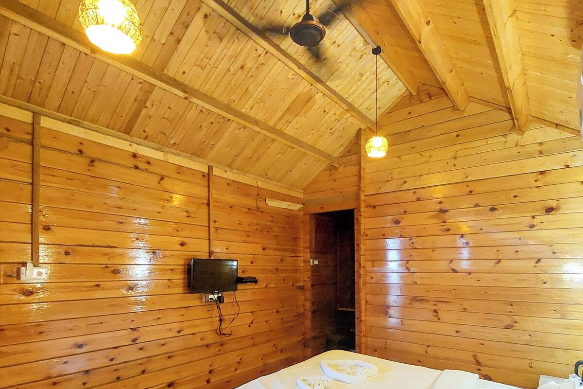 Une pièce aux murs lambrés, équipée d’un lit, d’un ventilateur de plafond et d’un luminaire suspendu.