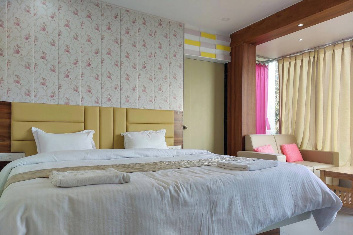 Une chambre d’hôtel avec un grand lit, une tête de lit en bois, un canapé et une fenêtre avec des rideaux.