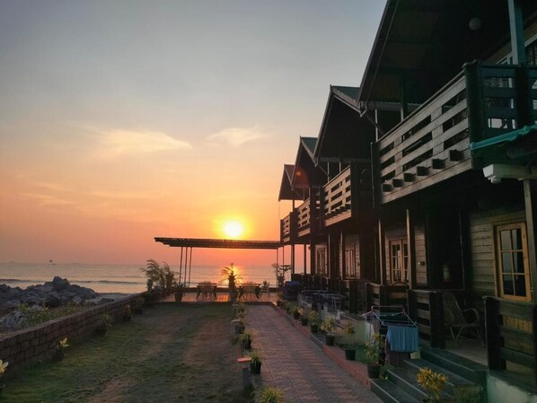 A wooden building with a covered patio overlooking the sea at sunset.