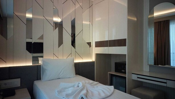 A modern hotel room with a neatly made bed, a bedside table, a built-in TV, and a small seating area. - Solis Boutique Hotel (Istanbul)