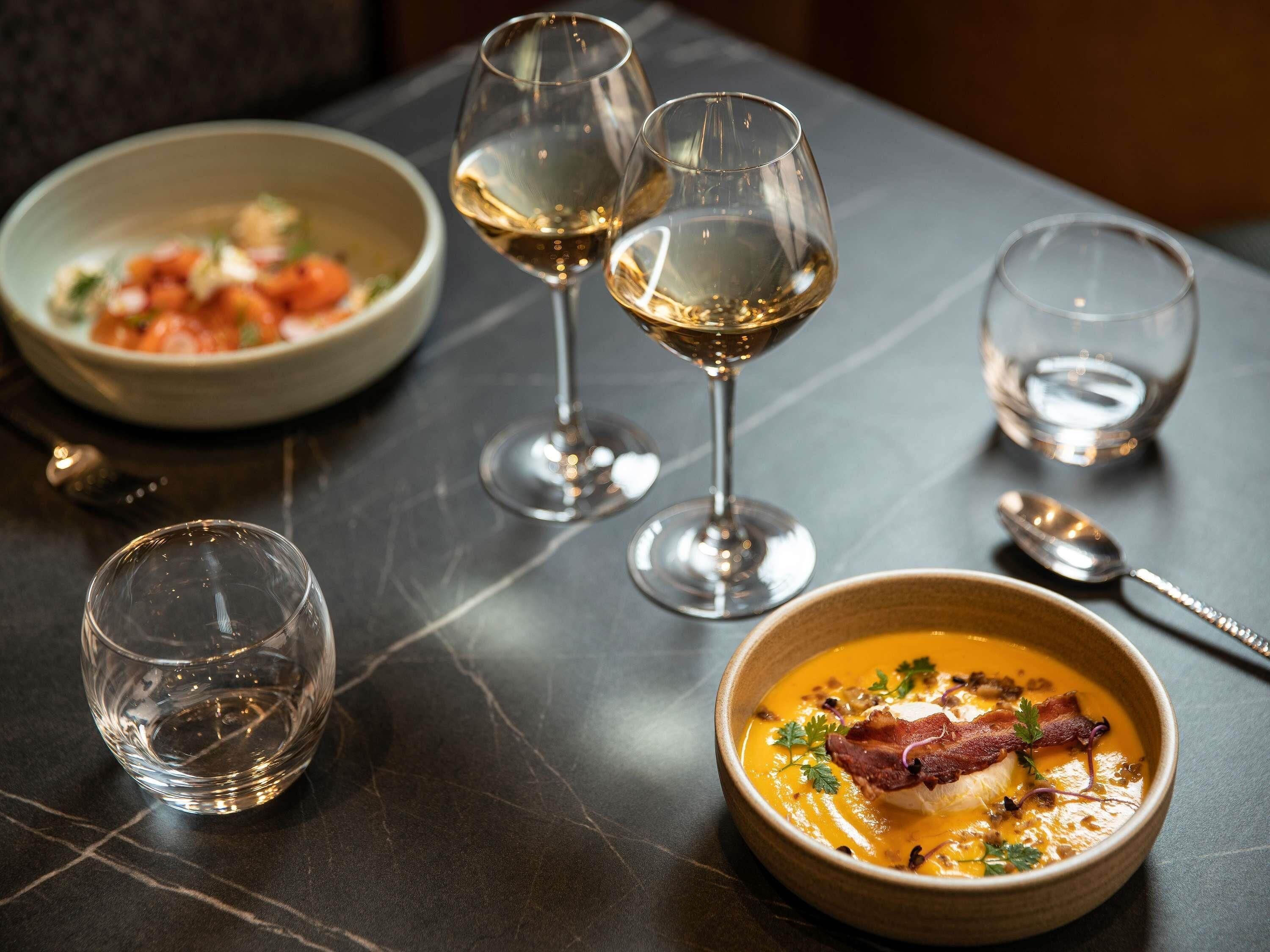 Una mesa con tres copas de vino, un tazón de sopa y una cuchara.