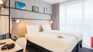 A hotel room with a large bed, a desk with a chair, a lamp, and artwork on the wall.