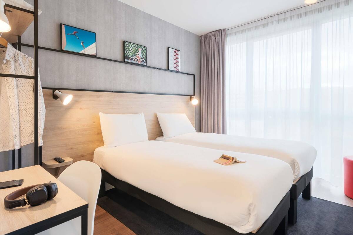 Et hotelværelse med en stor seng, et skrivebord med stol, en lampe og billedkunst på væggen.