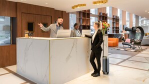A hotel reception area with a marble counter, modern lighting fixtures, and a seating area with a unique chair design.
