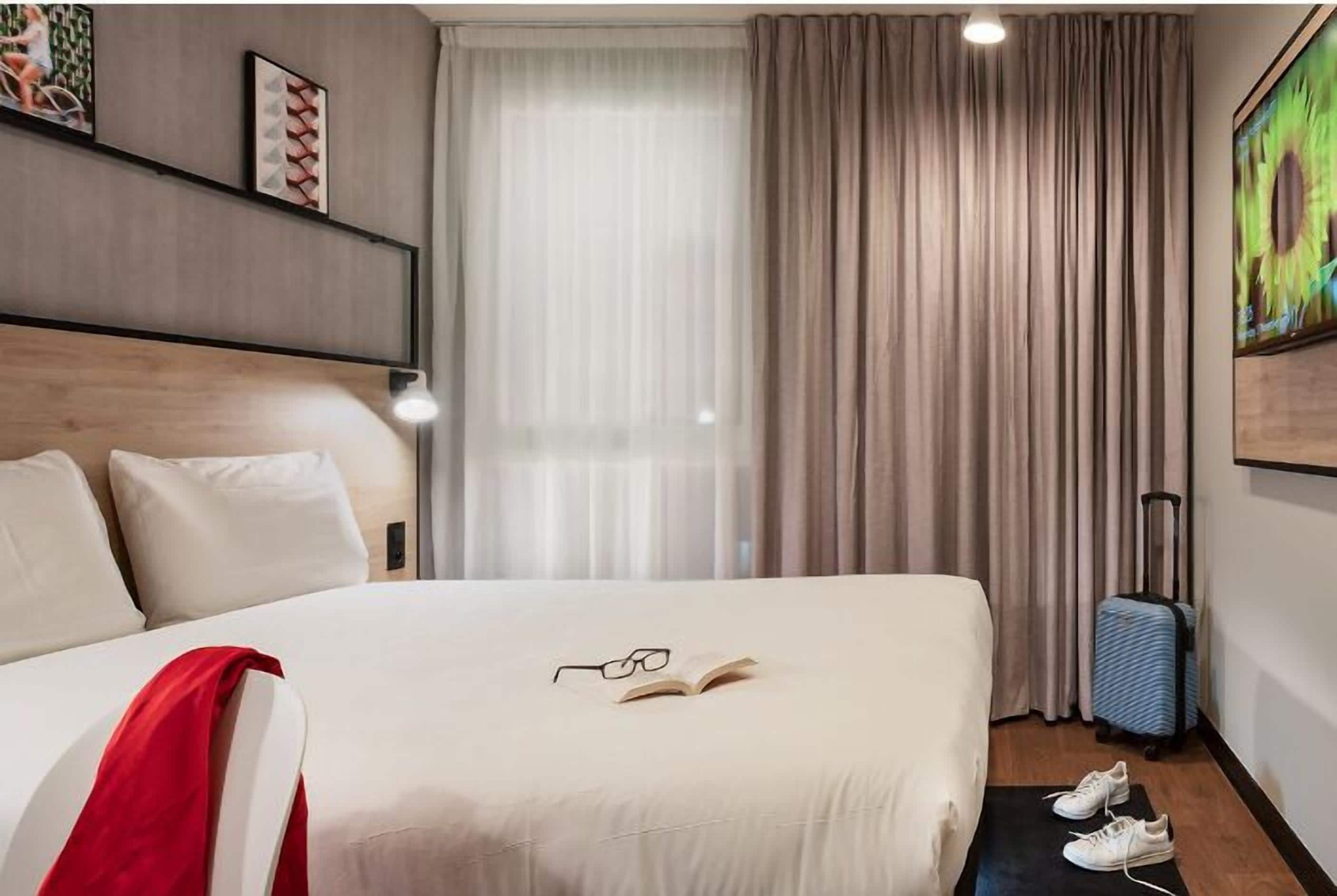 A hotel room with a bed, a suitcase, and a pair of shoes on the floor.