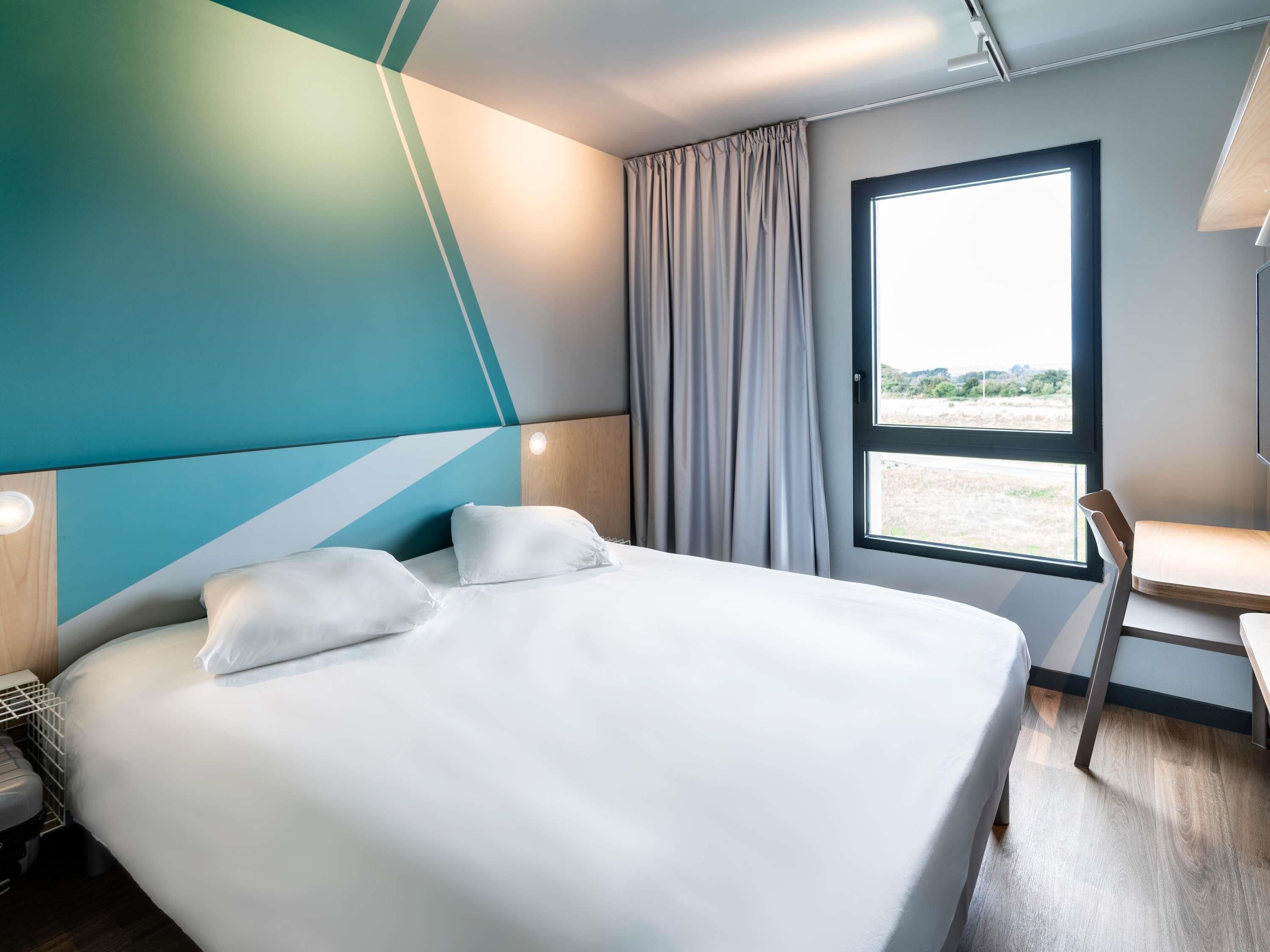 A modern hotel room with a large bed, a desk, and a window with a view.