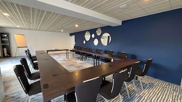 Un salón de conferencias con una mesa larga, múltiples sillas, una pizarra y una pared azul con espejos circulares.