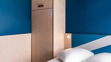 Ein kleines Zimmer mit einem Einzelbett, einem Holzschrank und einer Wandleuchte.