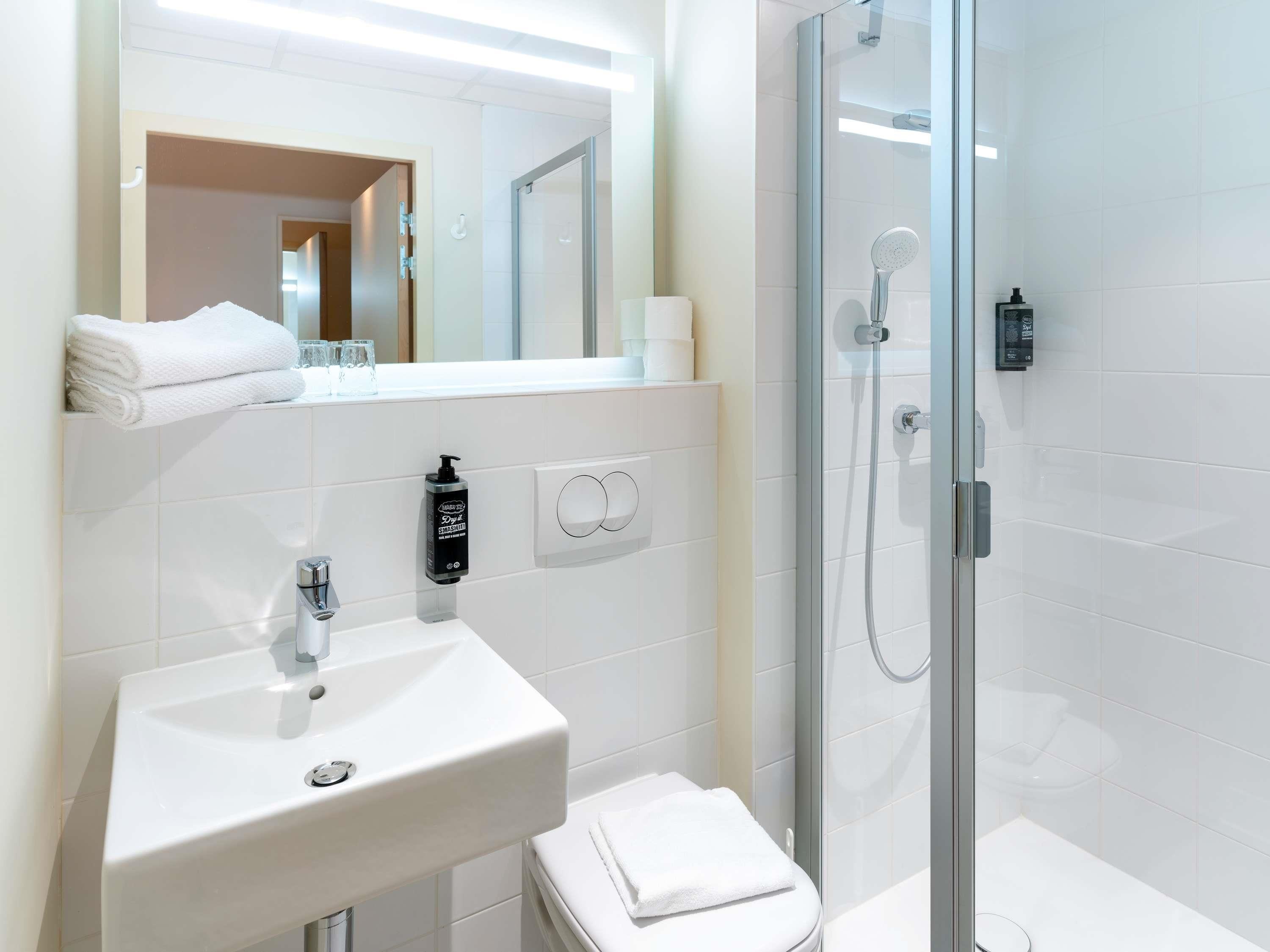 Un baño moderno con un lavabo blanco, ducha con mampara de vidrio y un espejo sobre el lavabo.
