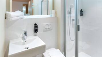 Un baño moderno con un lavabo blanco, ducha con mampara de vidrio y un espejo sobre el lavabo.