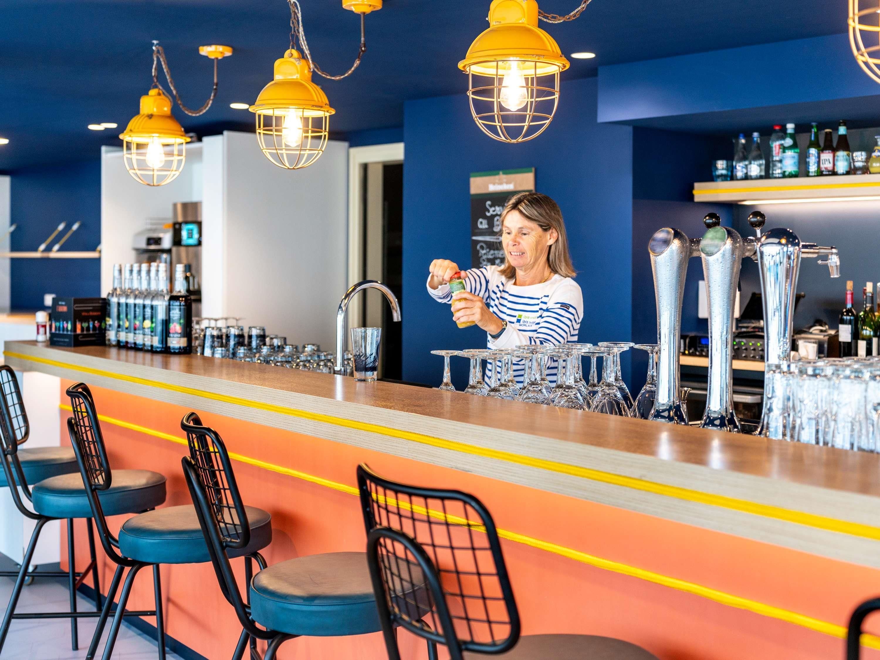 A bar area with a bartender preparing drinks, bar stools, and a variety of bottles on shelves.