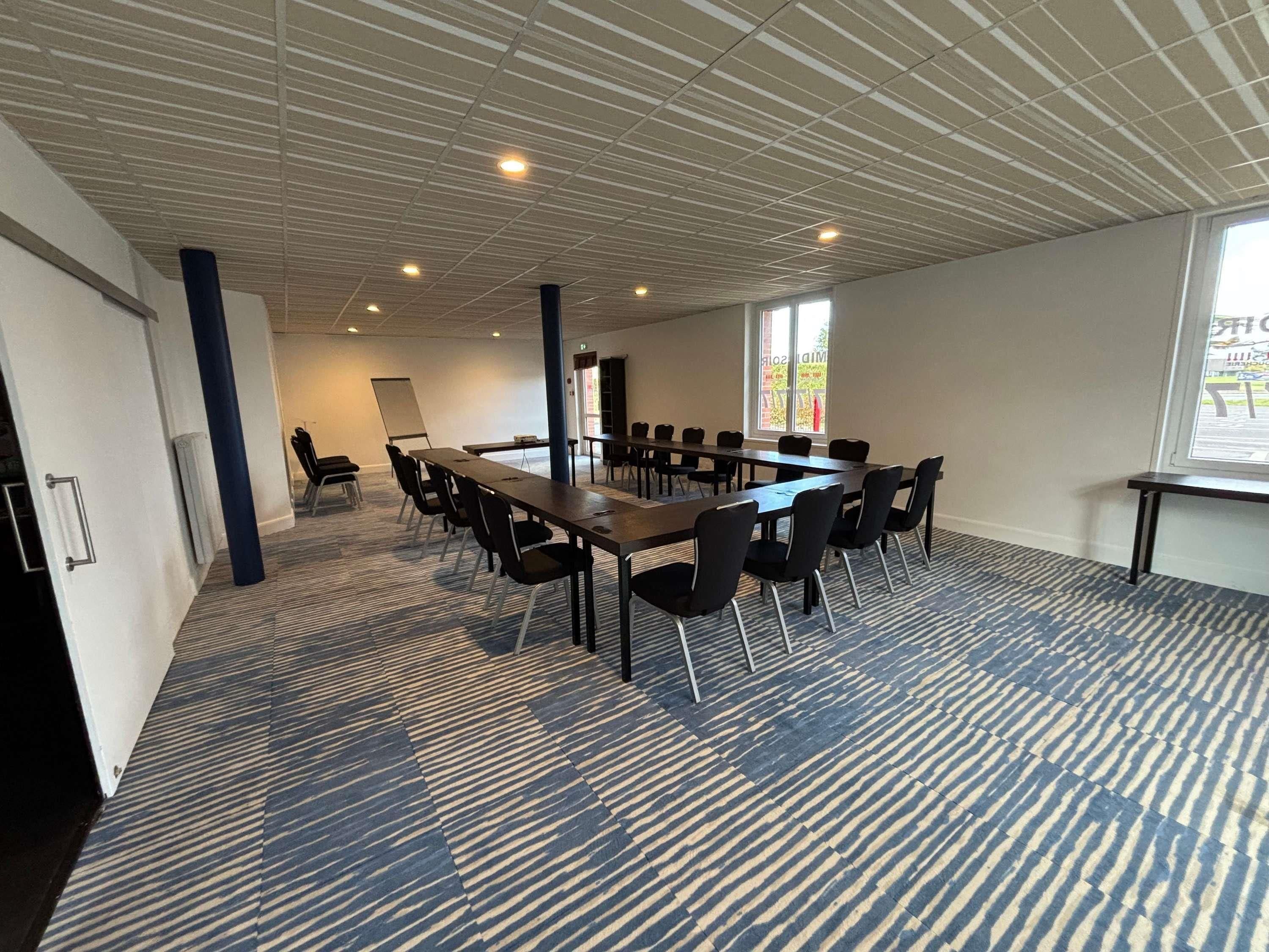 Une salle de conférence équipée d’une longue table, de chaises, d’un tableau blanc et d’un écran de projection.