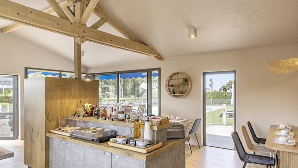 Une cuisine moderne avec un îlot central en bois, de grandes fenêtres et un coin repas avec des chaises.