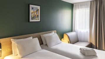 Ein Hotelzimmer mit einem Bett, einem Sessel, einem Bild an der Wand und einem Fenster mit Vorhängen.