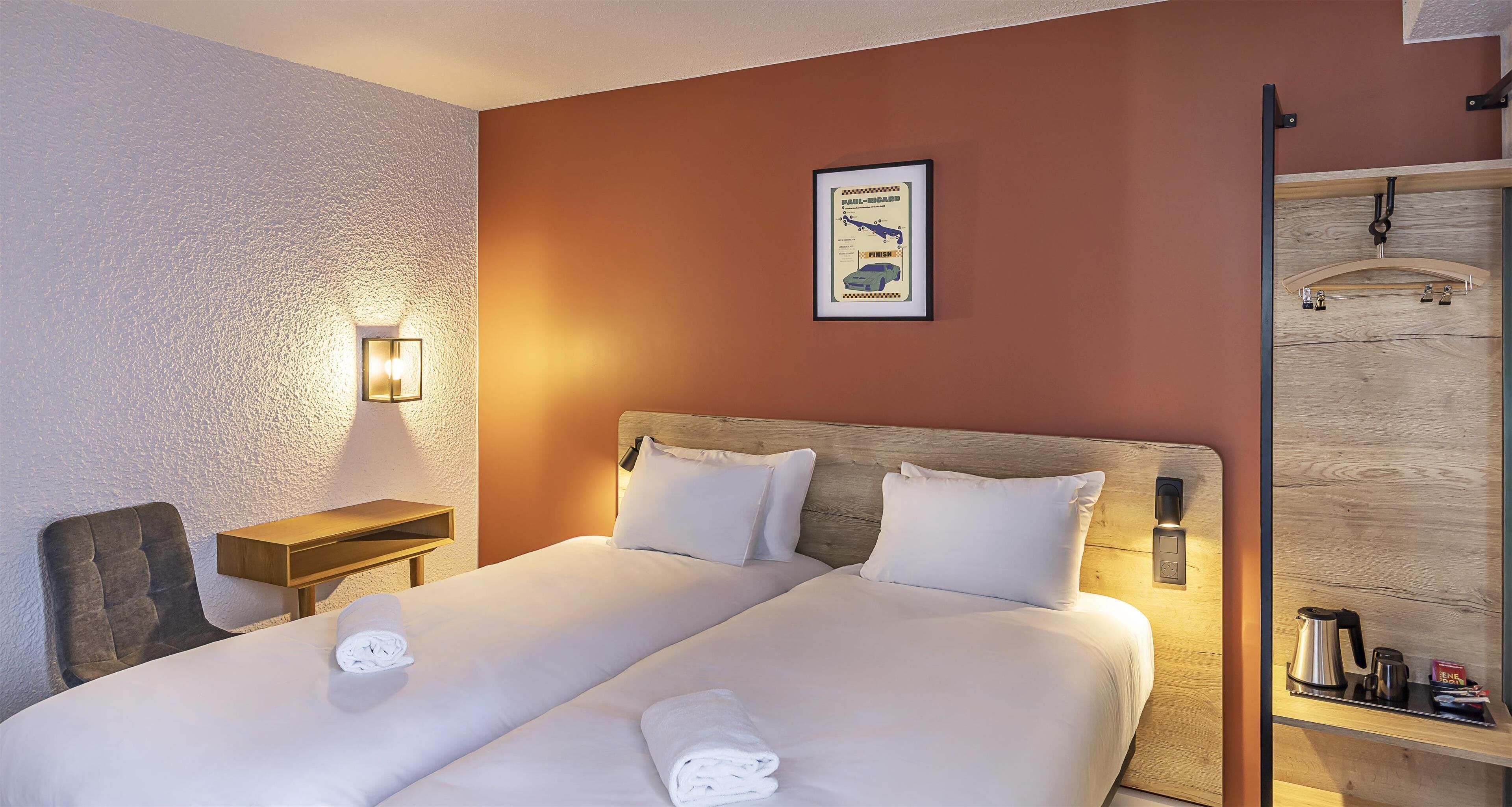 Un lit double avec du linge de lit blanc et deux oreillers, une tête de lit en bois, une table de chevet avec une lampe et une carte encadrée accrochée au mur.