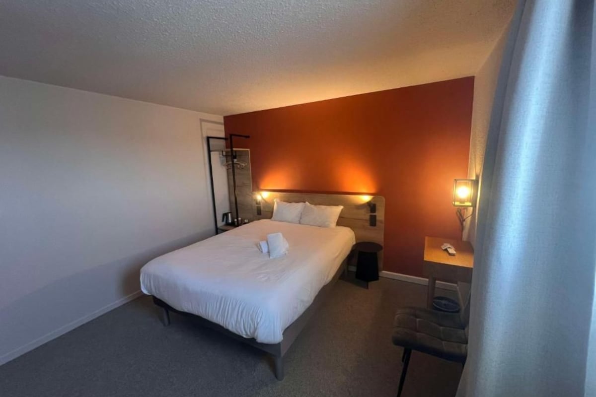 Una habitación de hotel con una cama, mesitas de noche, un escritorio y una silla.