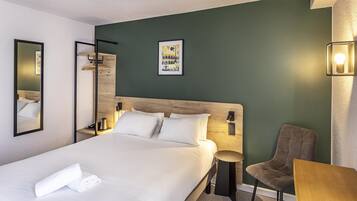 Une chambre d’hôtel avec un grand lit, une chaise, une petite table et un luminaire fixé au mur.