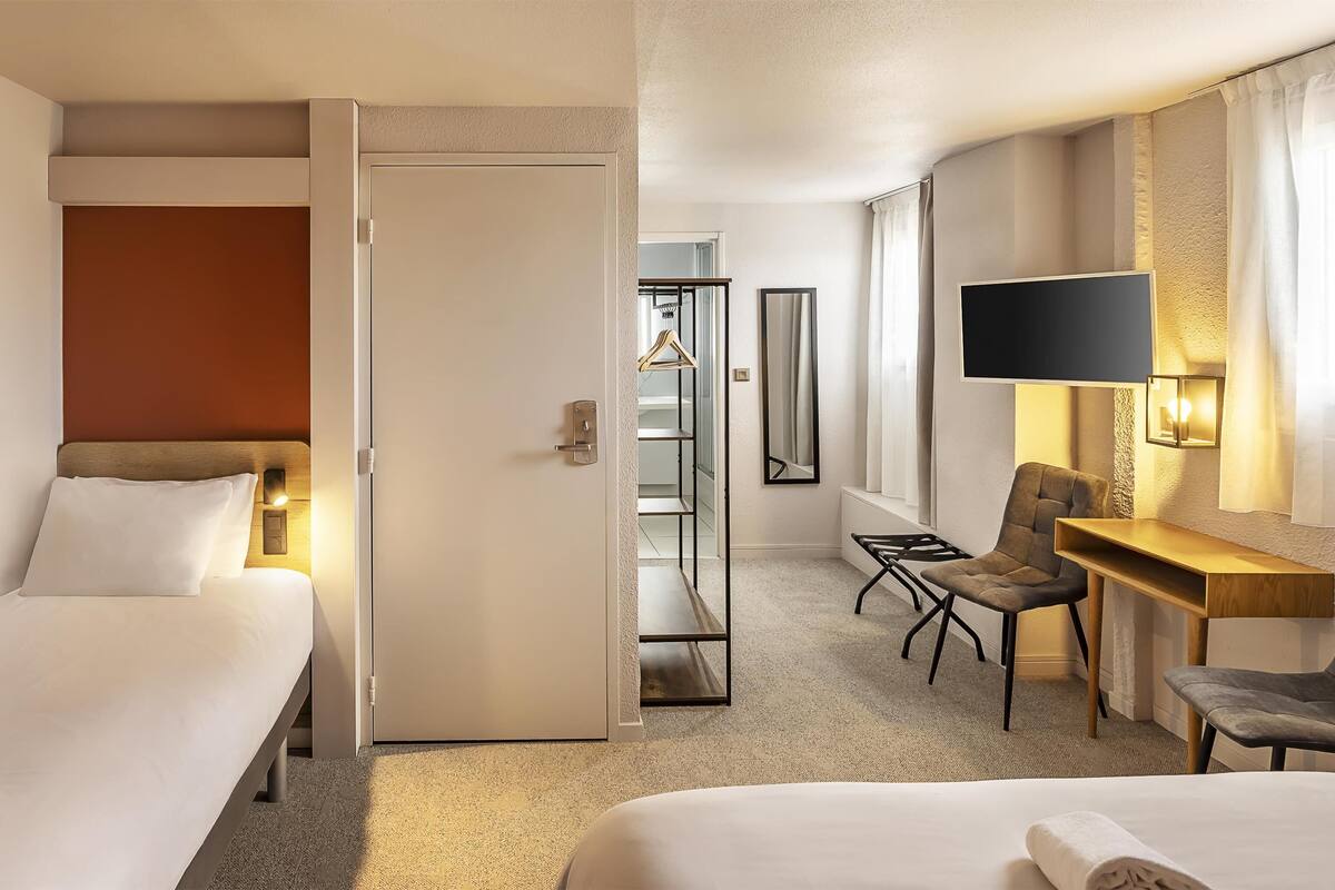 Une chambre d’hôtel avec deux lits, un bureau, une chaise, une télévision et une armoire.