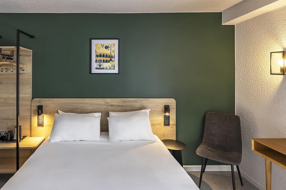 Une chambre d’hôtel comprenant un lit, une table de chevet, une chaise et une étagère fixée au mur.