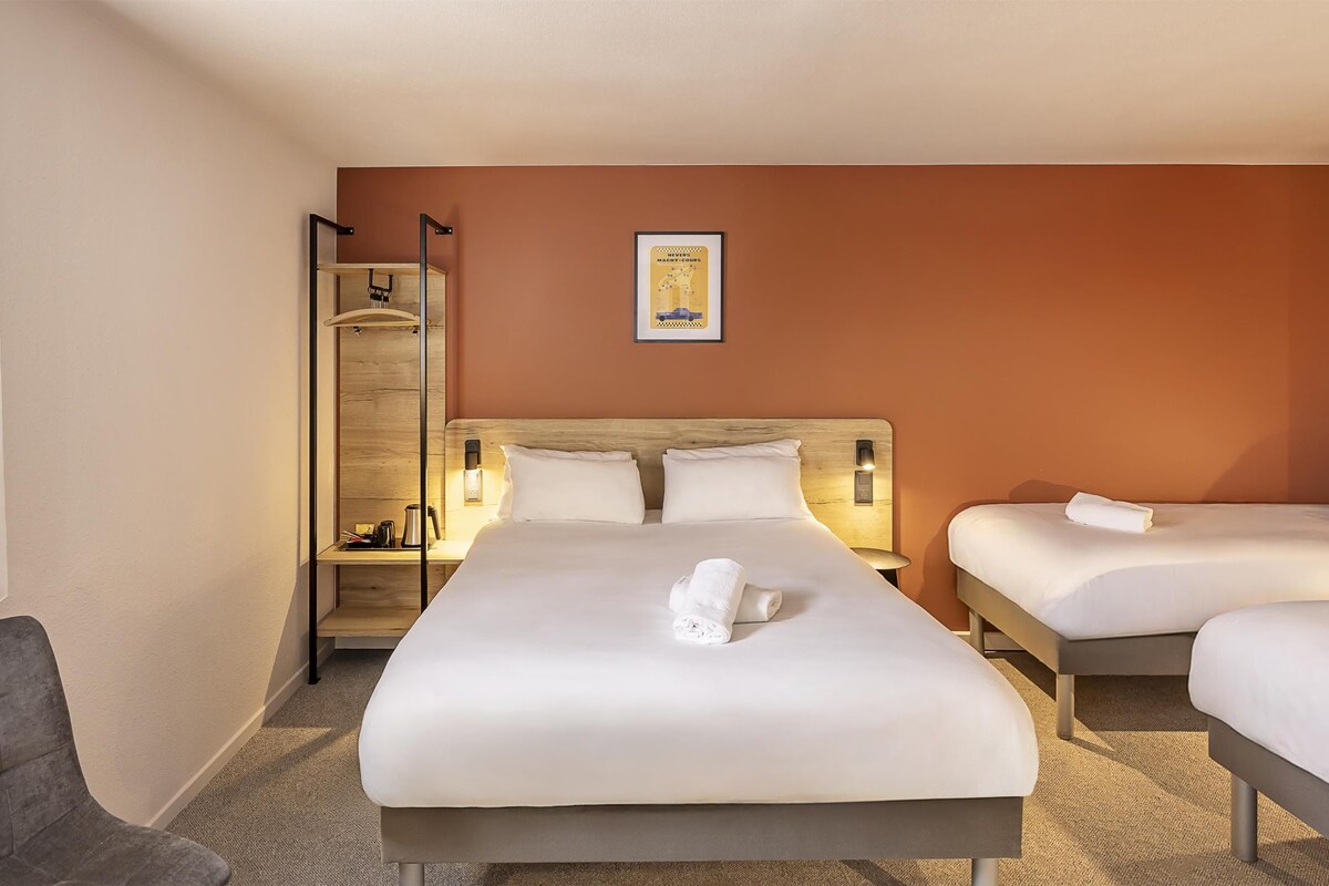 A hotel room with a large bed, two smaller beds, a sofa, a nightstand, a mirror, and a framed picture on the wall.