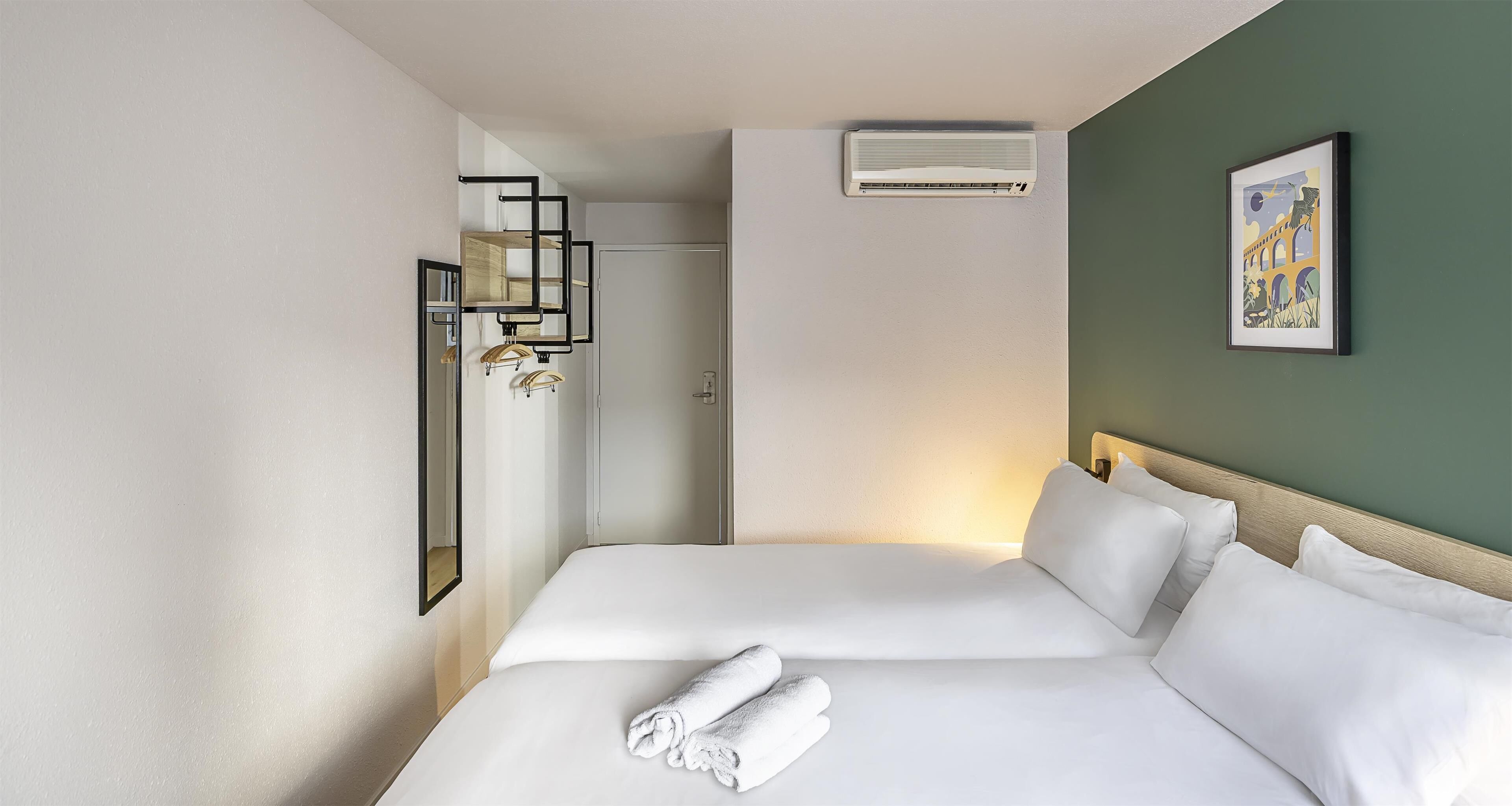 Habitación de hotel con dos camas, un espejo, un equipo de aire acondicionado y un cuadro en la pared.