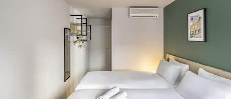 Habitación de hotel con dos camas, un espejo, un equipo de aire acondicionado y un cuadro en la pared.