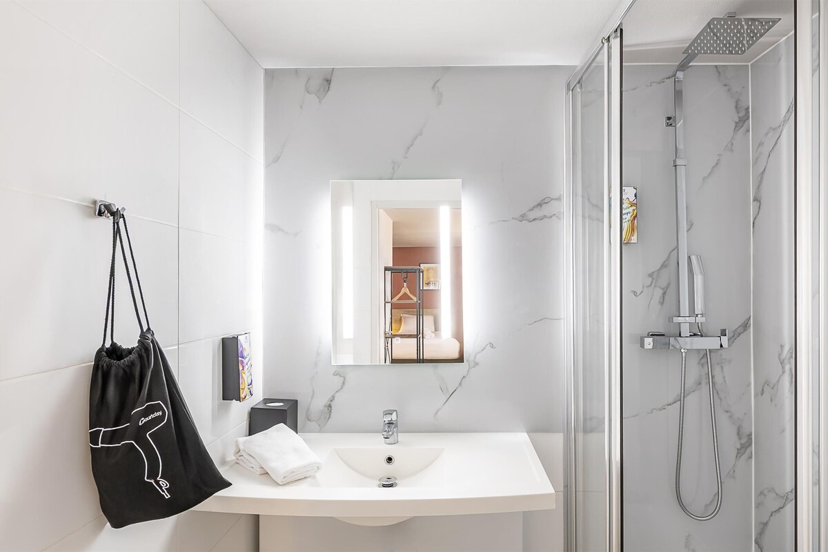 Un baño moderno con lavamanos de mármol, ducha con mampara de vidrio y toalla colgante.