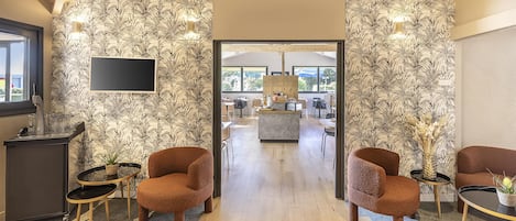 En modern hotellobby med en central sittgrupp, en receptionsdisk och utsikt över matsalen.