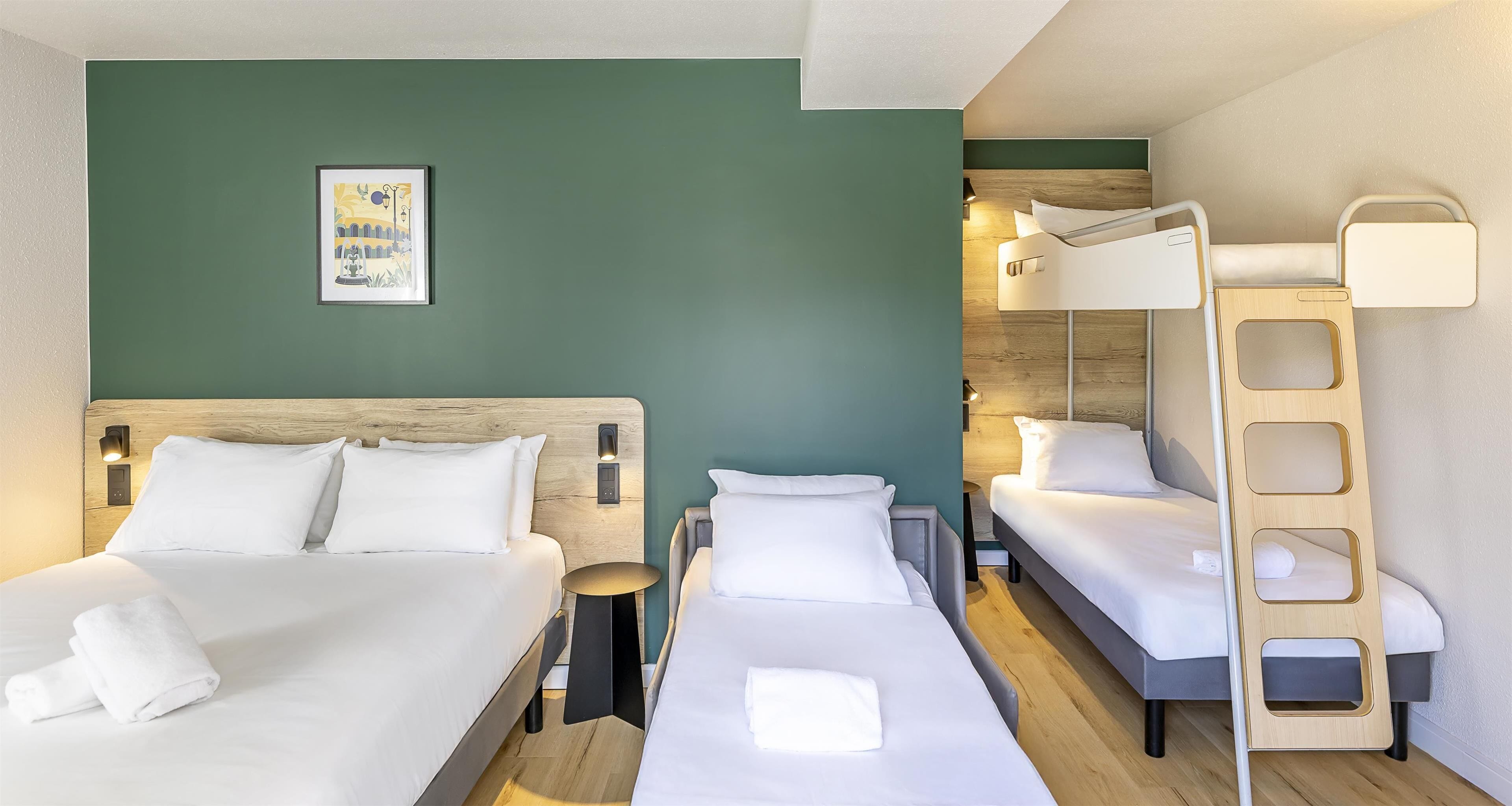 A hotel room with two beds, a bunk bed, a wooden ladder, and a wall-mounted light fixture.