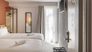 Une chambre d’hôtel avec deux lits, un grand miroir, une armoire et une vue sur la ville à travers des rideaux transparents.