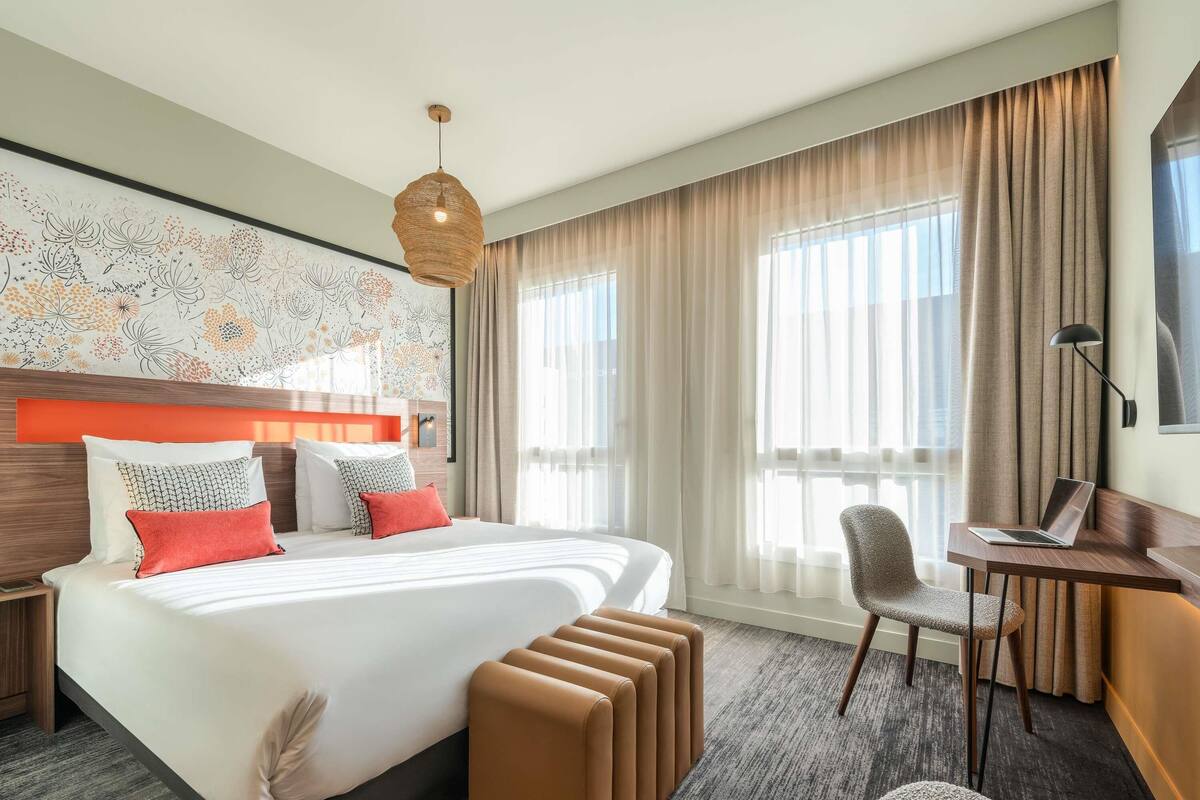 Une chambre d’hôtel avec un grand lit, un bureau, une chaise, un ordinateur portable et une vue sur l’extérieur.