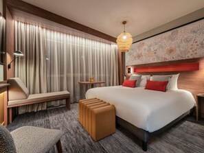 Ein Hotelzimmer mit einem großen Bett, einer Bank, einem kleinen Tisch und einer Pendelleuchte.