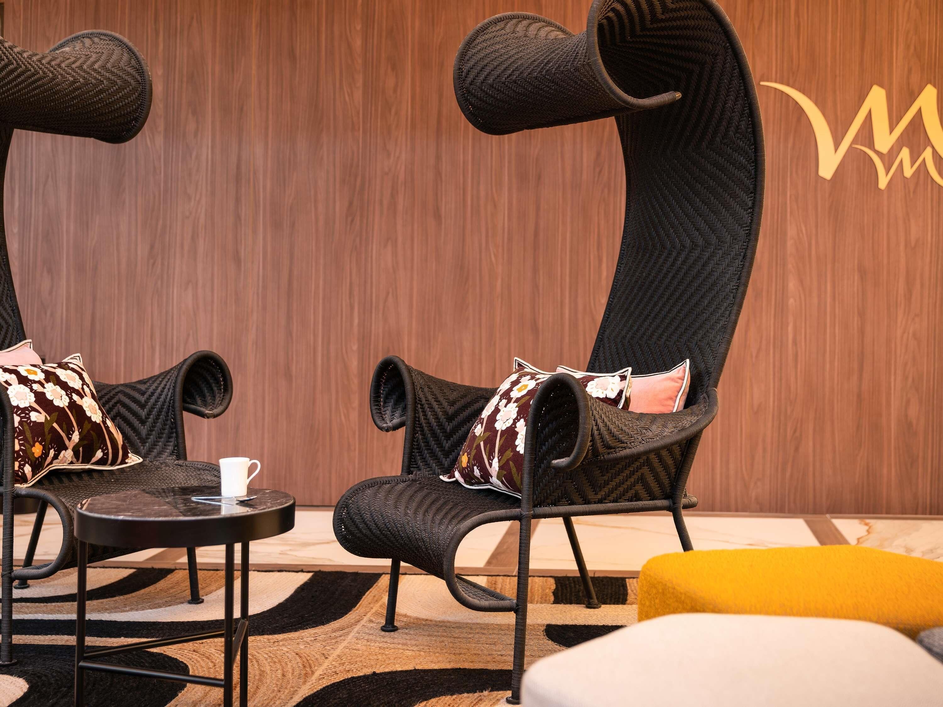 Une pièce avec deux fauteuils aux formes arrondies, une petite table sur laquelle se trouve une tasse, et un pouf jaune.
