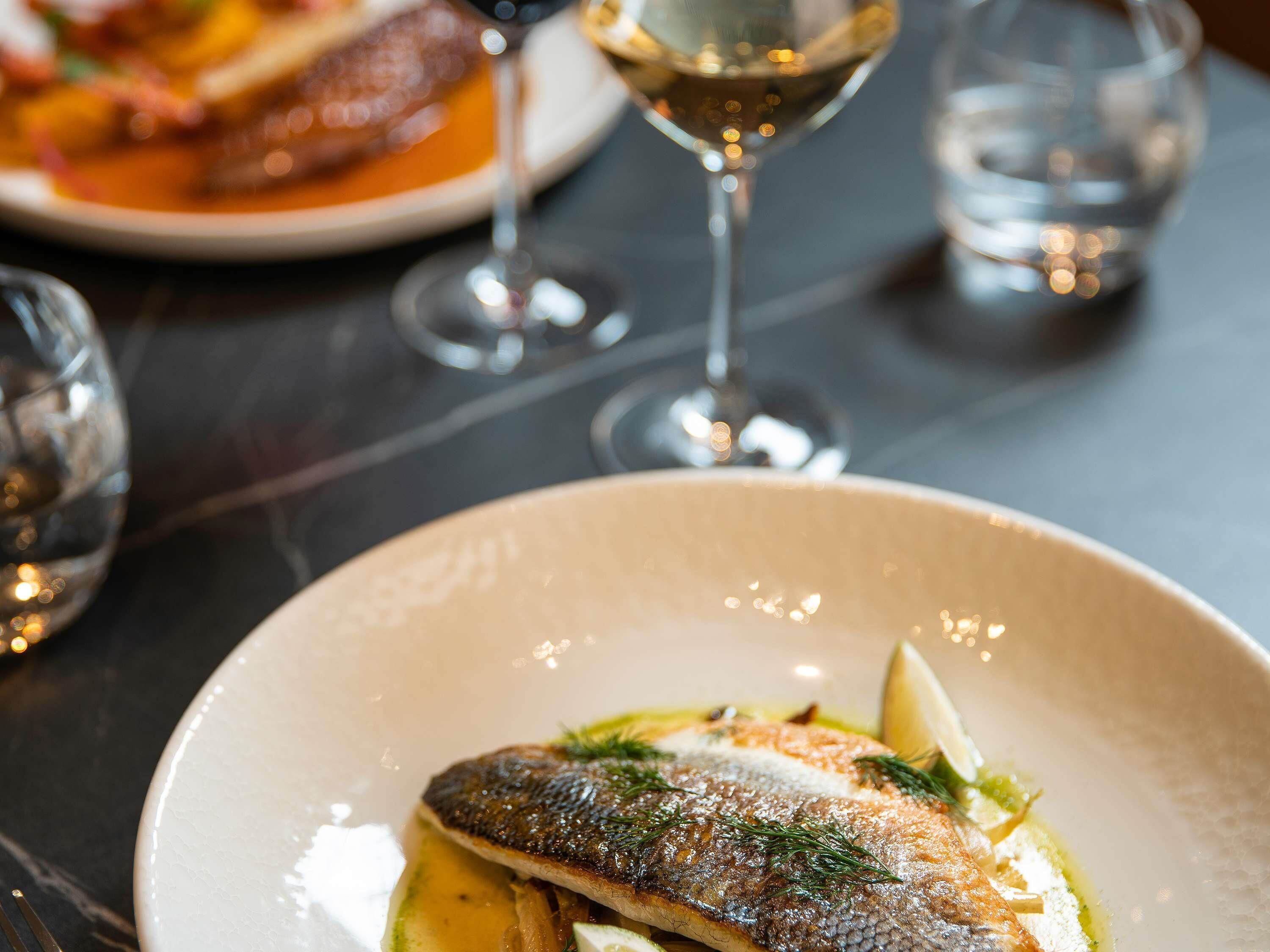A dining table with a plate of fish, a glass of white wine, and a glass of water.