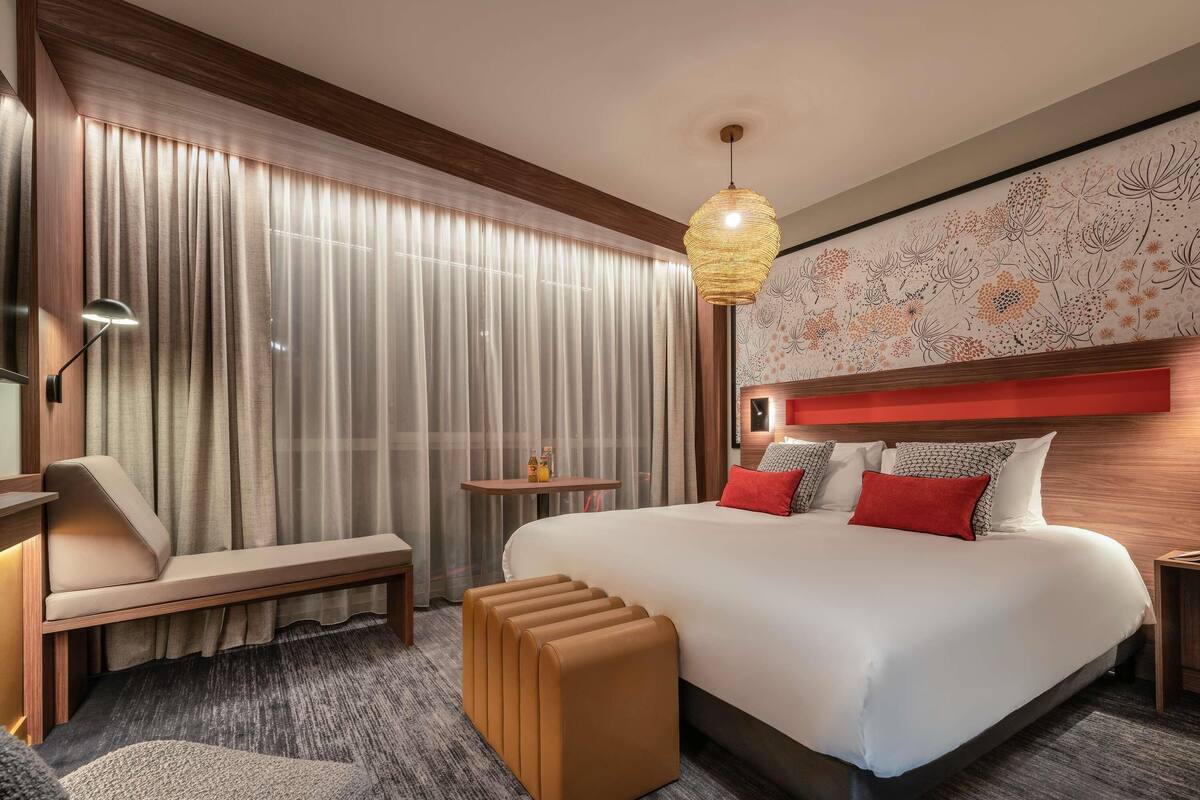 Une chambre d’hôtel avec un grand lit, un banc, une petite table et un mur décoratif.