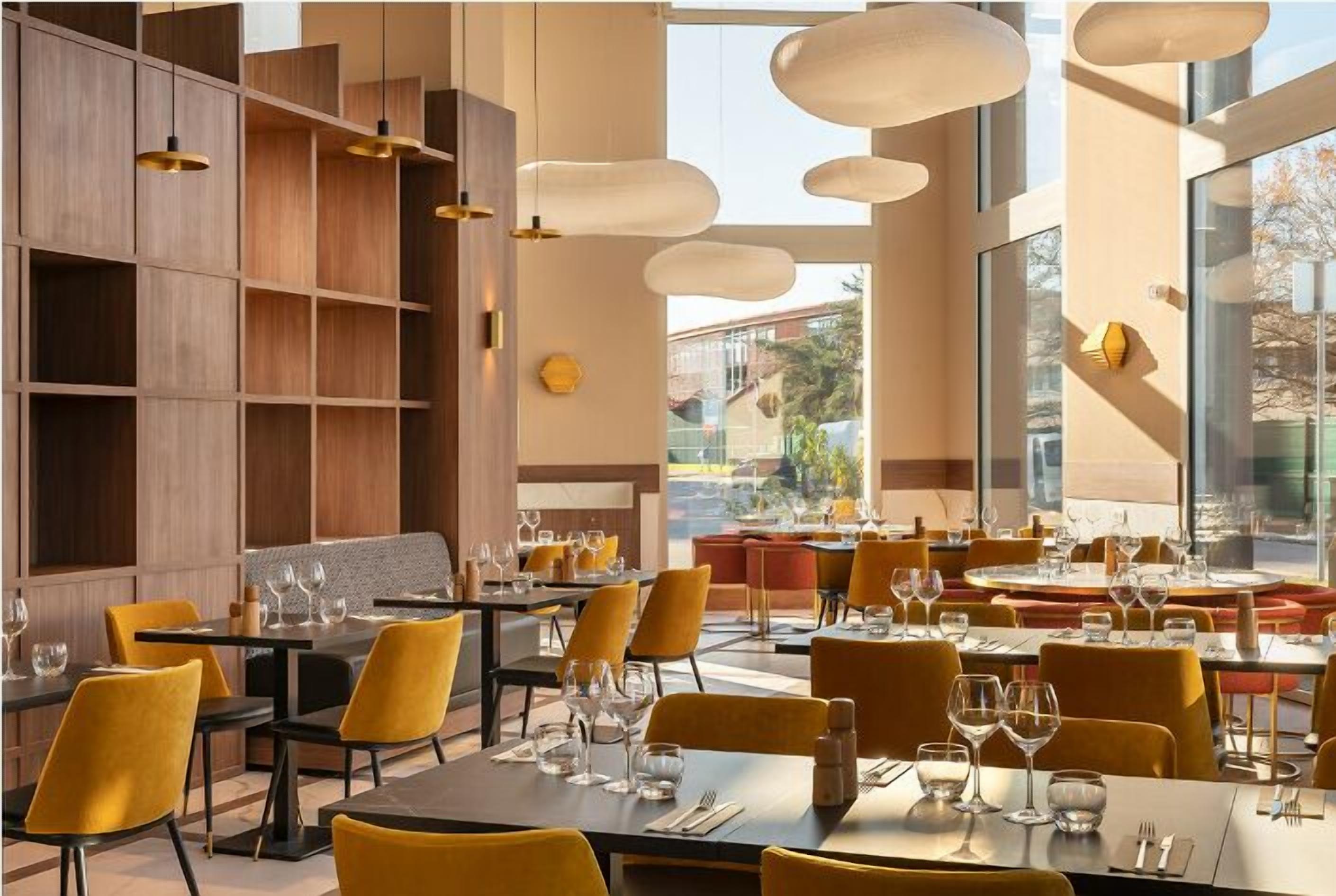 A restaurant with tables set for dining, yellow chairs, and hanging pendant lights.