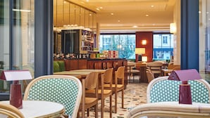 A café with wicker chairs and tables, a coffee machine, and a view of the outside. - Mercure Paris Butte Montmartre Basilique (Paris)