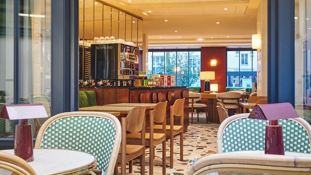 A café with wicker chairs and tables, a coffee machine, and a view of the outside. - Mercure Paris Butte Montmartre Basilique (Paris)
