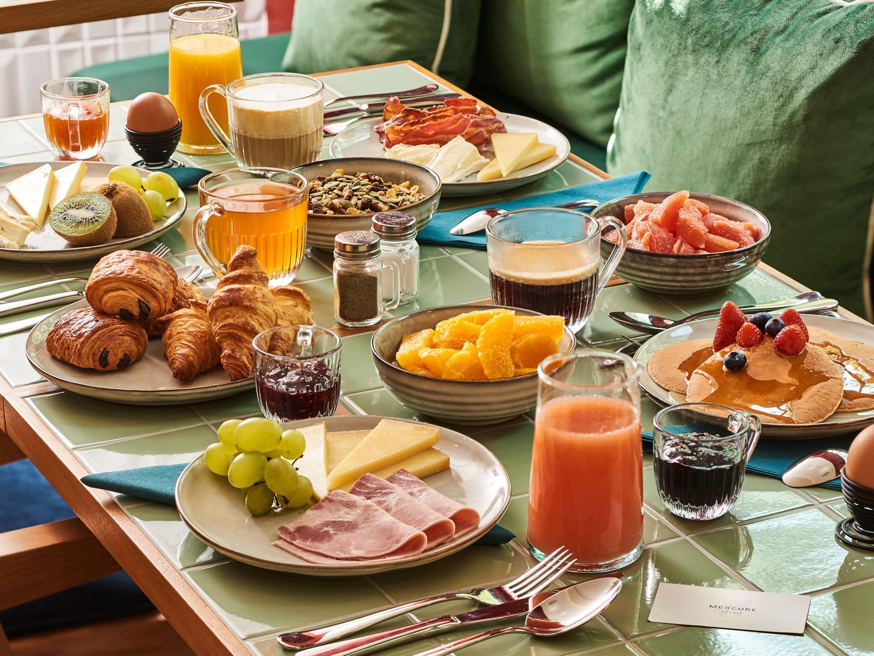 A breakfast table with croissants, cheese, ham, fruit, and beverages.