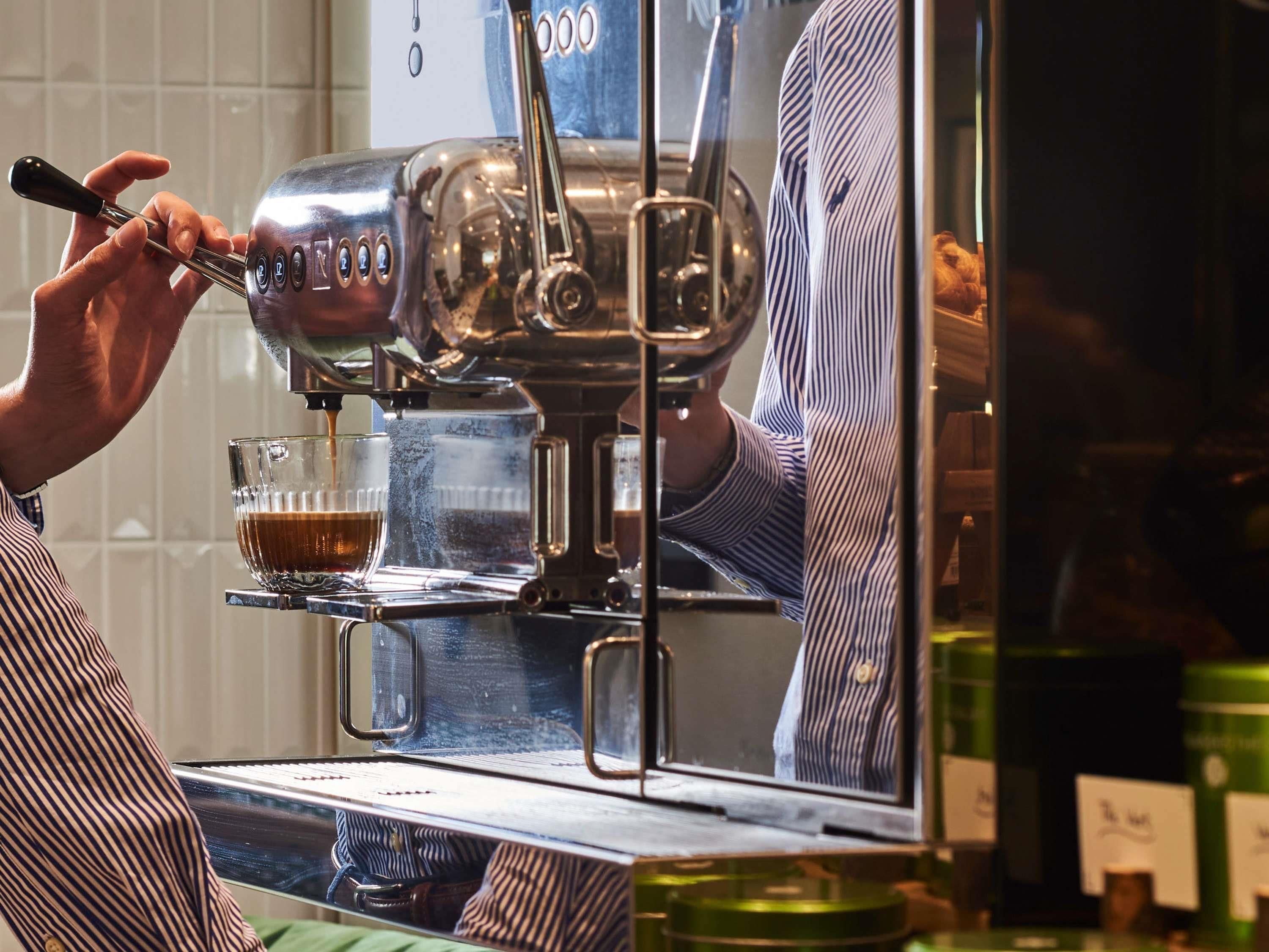 A person using a coffee machine, with a glass cup and a spoon.