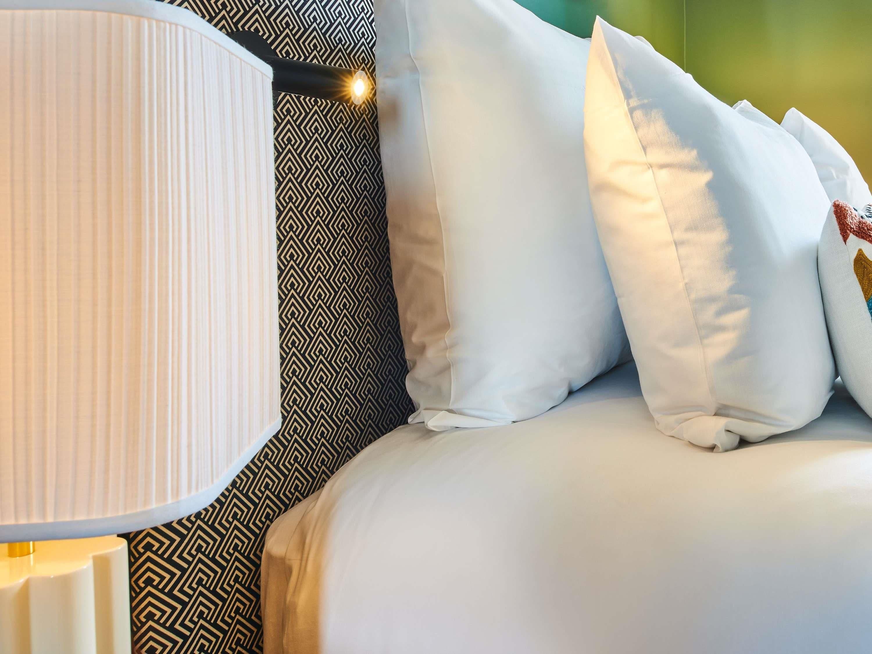 A neatly made bed with white bedding and a patterned pillow.