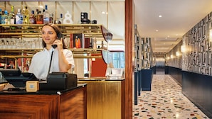 A bar area with a wooden counter, a cash register, and a computer. There are shelves with bottles and glasses behind the counter. - Mercure Paris Butte Montmartre Basilique (Paris)